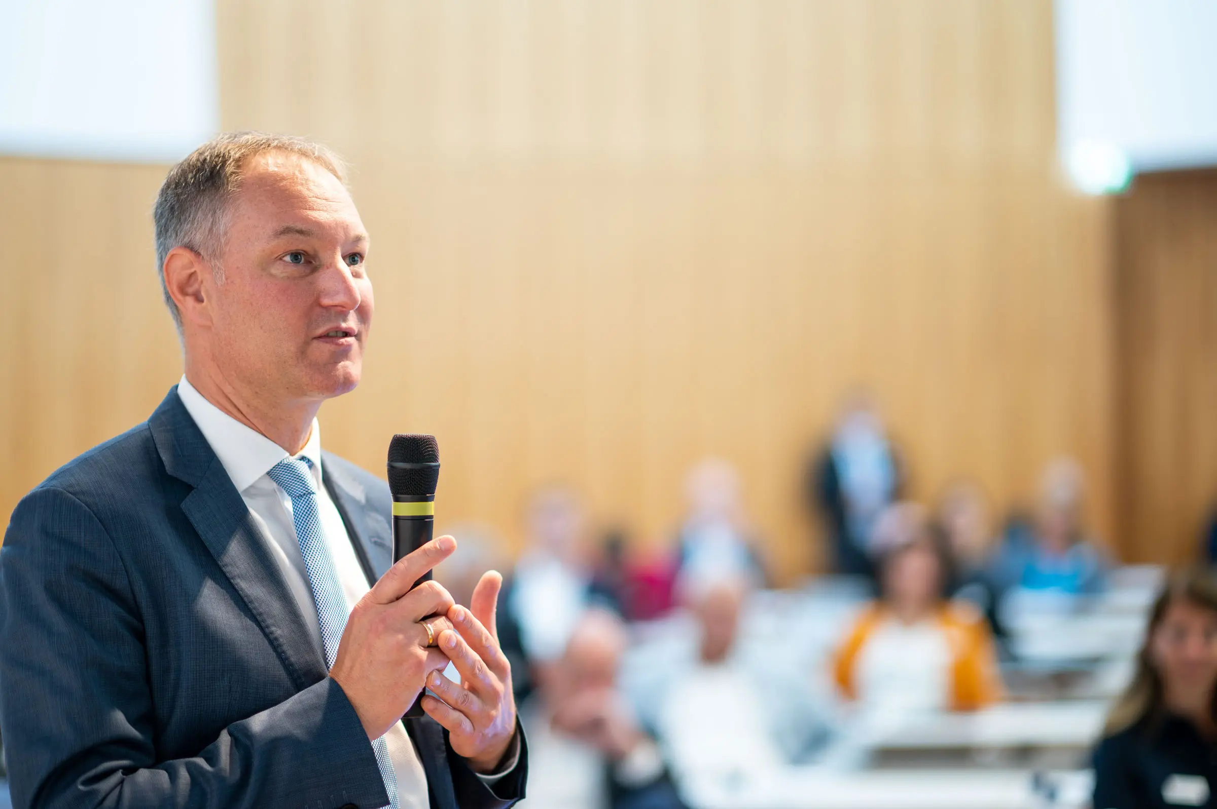Redner während eines Vortrags vor unscharf erkennbarem Publikum